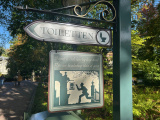 <a href="/lemma/Toilet" title="Toilet">Toilet</a>-wegwijzer bij <a href="/lemma/%27t_Gemack" title="&#039;t Gemack">&#039;t Gemack</a>, een jongen met pet rent naar het toiletgebouw, ook te zien is de ganzen-<a href="/lemma/Drinkfontein" title="Drinkfontein">drinkfontein</a> en op de achtergrond een zuil van het hek van <a href="/lemma/Kindervreugd" title="Kindervreugd">Kindervreugd</a>. Binnen in het gebouw lijkt de toiletstoel te staan die ook op het gevelbord van het gebouw te zien is.