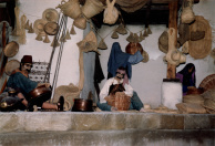 Eerste Marktscène, 12-1985. Het eerste deel aan de rechterzijde van de Marktscène, rijkelijk bezaaid met rekwisieten. De gezichten zijn theatraal opgemaakt om goed uit te komen in de contrastrijke showverlichting, met lichte accenten op de lichtvangende delen van de gezichten.