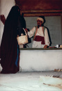 Eerste Marktscène, 06-1985. Close-up van de fruitverkoper (met paprika) en de gesluierde vrouw (maiskolf). Op de toonbank allerhande rommel, van kniptangetjes tot koffiebekertjes. Op de grond een afgevallen handje.