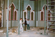 Troonzaal, 10-1985. De hoek van de Troonzaal waar de Pasha op zijn verhoging zit, gefotografeerd vanuit de plek waar tegenwoordig diens gasten zitten. Links in de hoek zien we witte lichaamsdelen van de Djinn.  Alle pilaren krijgen nog decoratieve ombouwen met marmer-imitatie en daartussen komt nog de trapsgewijze verhoging. Alle ramen worden voorzien van glas-in-lood-imitatie en behangen met Aziatisch behang, bij gebrek aan niet-leverbaar Oosters behang.