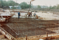 Exterieur, 05-1984. Beton wordt gestort. Op de achtergrond een tijdelijke werkplaats en dito 'nissenhut' waar verschillende technieken door o.a. Mari van Heumen en Henk Smulders gemaakt worden. Het bruine houten schuurtje is een overblijfsel van de voormalige manege, die later plaats maakt voor het voorplein van de attractie.