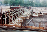 Exterieur, 05-1984. We zien vermoedelijk de fundering voor de buitenmuren aan de voorste hoek van het gebouw, nabij de Bazaar. Links in de achtergrond het Roeivijver-huisje nabij de Veulenweide. Het geheel is afgezet met bouwhekken. Aan de andere kant van de Veulenweide wordt over enkele maanden gestart met de bouw van de Bob.