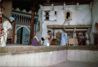 Tweede Marktscène, 02-1986. De tweede marktscène enkele maanden voor opening. Voornamelijk rekwisieten missen nog, zoals de vele (lichtgevende) flessen van de flessenverkoper, waardoor we de simpele houten constructie van zijn tafeltje nog zien. Mogelijk mist de jongen met kruik op zijn hoofd, of valt deze net buiten de foto. Op de vloer schuin achter de tapijtverkoper komt later het zwevend tapijt.