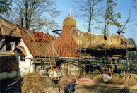 Veel dakwerkzaamheden met verschillende materialen bij Lal's Brouwhuys. Links worden leien gelegd, rechts rietgedekt, en een aantal dakdelen is al voltooid. De muren zijn inmiddels gestuct.