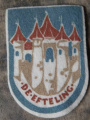 Efteling-souvenir jaren vijftig, een patch om op je kleding te naaien met het kasteeltje van <a href="/lemma/Doornroosje" title="Doornroosje">Doornroosje</a> met vaandel &quot;De Efteling&quot;, ontworpen door <a href="/lemma/Henk_Potters" title="Henk Potters">Henk Potters</a>.
