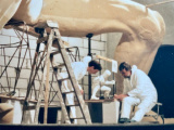 Vormgevers <a href="/lemma/Hans_Pulles" title="Hans Pulles">Hans Pulles</a> en <a href="/lemma/Adriaan_Derksen" title="Adriaan Derksen">Adriaan Derksen</a> bestuderen het model van de &#039;Djinno&#039; (<a href="/lemma/Djinn" title="Djinn">Djinn</a>) voor <a href="/lemma/Fata_Morgana" title="Fata Morgana">Fata Morgana</a> terwijl de uitgewerkte Djinn boven hen uittorent.