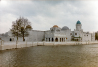 Exterieur, 04-1985. Zicht op de voorgevel, met nog maar weinig delen in de juiste kleuren afgewerkt en ingeschaduwd. Uiteindelijk wordt één van de twee bomen aan deze zijde nog verwijderd.