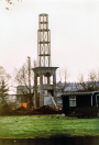 Exterieur, 03-1985. De constructie van de minaret bij ochtendgloren, in de voorgrond een bouwkeet met geparkeerd 'dienstvoertuig'.