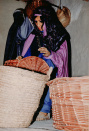 Eerste Marktscène, 12-1985. Close-up van de mandenvlechtende vrouw en daarachter de gesluierde dame die tussen de hangende manden neust.