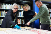 Conservator Textielmuseum Sjouk Hoitsma, Efteling-kledingontwerper <a href="/lemma/Carla_de_Kroon" title="Carla de Kroon">Carla de Kroon</a> en Efteling-grafisch ontwerper <a href="/lemma/Jasper_Douenburg" title="Jasper Douenburg">Jasper Douenburg</a> bekijken ontwerpen van <a href="/lemma/Anton_Pieck" title="Anton Pieck">Anton Pieck</a> voor damast voor het koninklijk huis uit de collectie van het museum, ter inspiratie voor een Efteling <a href="/lemma/Tafellinnen-set" title="Tafellinnen-set">tafellinnen-set</a>.