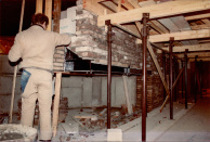 Krokodillentunnel, 03-1985. Cees Bouwens metselt aan een overstekende bakstenen wand vlak boven het wateroppervlakte in de krokodillentunnel, om zo de scherpe bocht naar rechts te kunnen verhullen. De draaischijven waarover de kabel die de boten vooruit trekt in de vaargeul loopt zijn rond met een forse diameter en moeten hier onderdoor kunnen draaien. Ten tijde van het ontwerp van de lay-out was men nog van plan een 'wegvarende' boot rechtdoor achter de krokodillen te plaatsen om de suggestie te wekken dat de boot met gasten door de krokodillen moest varen. Door de rechtdoor lopende gemetselde muur moest het langer een verrassing blijven dat de boten eigenlijk een bocht naar rechts zullen maken.