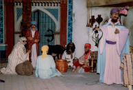 Tweede Marktscène, 02-1986. Close-up van de flessenverkoper en het groepje toeschouwers rondom de fakir met slangenmand. We zien nu ook goed het ezeltje achter hen, dat tegenwoordig lastiger te zien is, zeker omdat het ook nog bepakt is met manden en kleden.