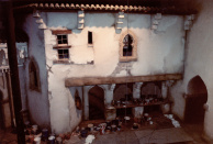 Tweede Marktscène, 05-1985. De balie van de marktkoopman in de tweede marktscène gezien vanuit de loopbrug achter de tegenover gelegen gevel. Het decoratieve schilderwerk van deze gevel is afgerond, aan de linkerzijde zien we de decoratieve doorgang die nog in zijn basiskleur staat. Rechts de doorgang naar de eerste marktscène, waar de tandarts zijn patiënten helpt.