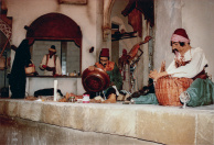 Eerste Marktscène, 06-1985. Mandenvlechter en koperslager in de Marktscène, en dier verschillende losse voeten daaromheen. Ook de groenteverkoper en de gesluierde vrouw zijn gearriveerd. In de achtergrond de voorbijlopende man, inclusief een rails met rijdende motor voor zijn loop-beweging, vergelijkbaar met de Monikkengang in het 7 jaar eerder geopende Spookslot. Aan de rechterzijde, onder het afdakje, de uitgeslepen paspop-achterzijde van de figuur die uiteindelijk aan de binnenzijde van het gesloten gordijn komt te staan.