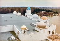 Exterieur, 04-1985. Het dak van het showgebouw, gezien vanaf de minaret. Inmiddels is de Vonderplas afgegraven tot aan de kademuren. Op de achtergrond goed zicht op de heuvel aan de Vonderplas met rechts de oorspronkelijke stenen brug, nog niet gestuct in de stijl van Fata Morgana zoals later het geval. Wel staat vlak voor de brug een tractor en is er een steiger naast de brug geplaatst, met daarnaast weer een roeiboot, wat kan duiden op een spoedige start met de upgrade van de brug in nieuwe stijl.