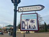 <a href="/lemma/Toilet" title="Toilet">Toilet</a>-wegwijzer bij <a href="/lemma/Fata_Morgana" title="Fata Morgana">Fata Morgana</a>. Een wat steviger figuur wandelt tussen de palmbomen richting een toiletgebouw, een tengere persoon en een kind zijn met iets meer snelheid erheen onderweg.